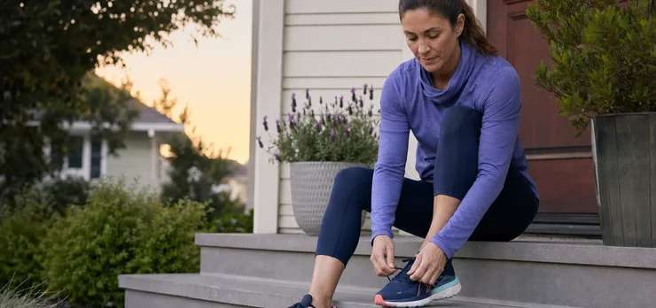 A woman lacing up her running shoes on her front step at dawn