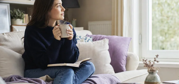 A woman on her sofa with a notebook and tea, thinking