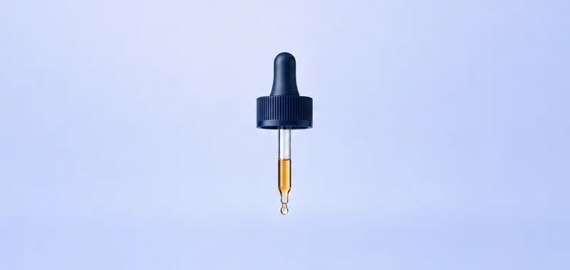 The glass dropper, with a single drop forming at the tip